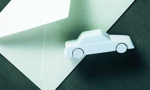 Ein graues Spielzeugauto liegt auf einem weißem Briefumschlag